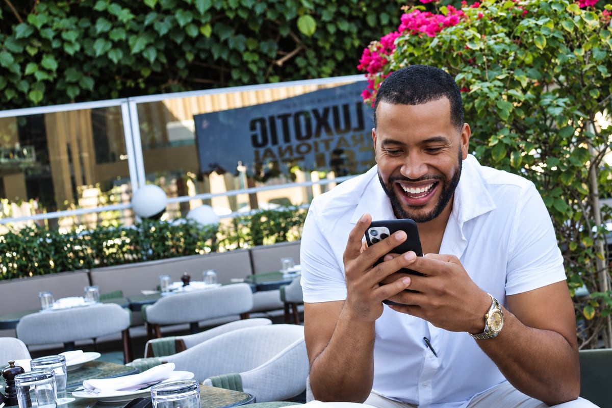 Armando laughing at his phone on a restaurant terrace in Dubai